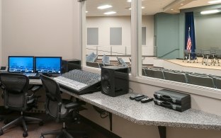 Audio control room behind a glass window overlooking an auditorium.