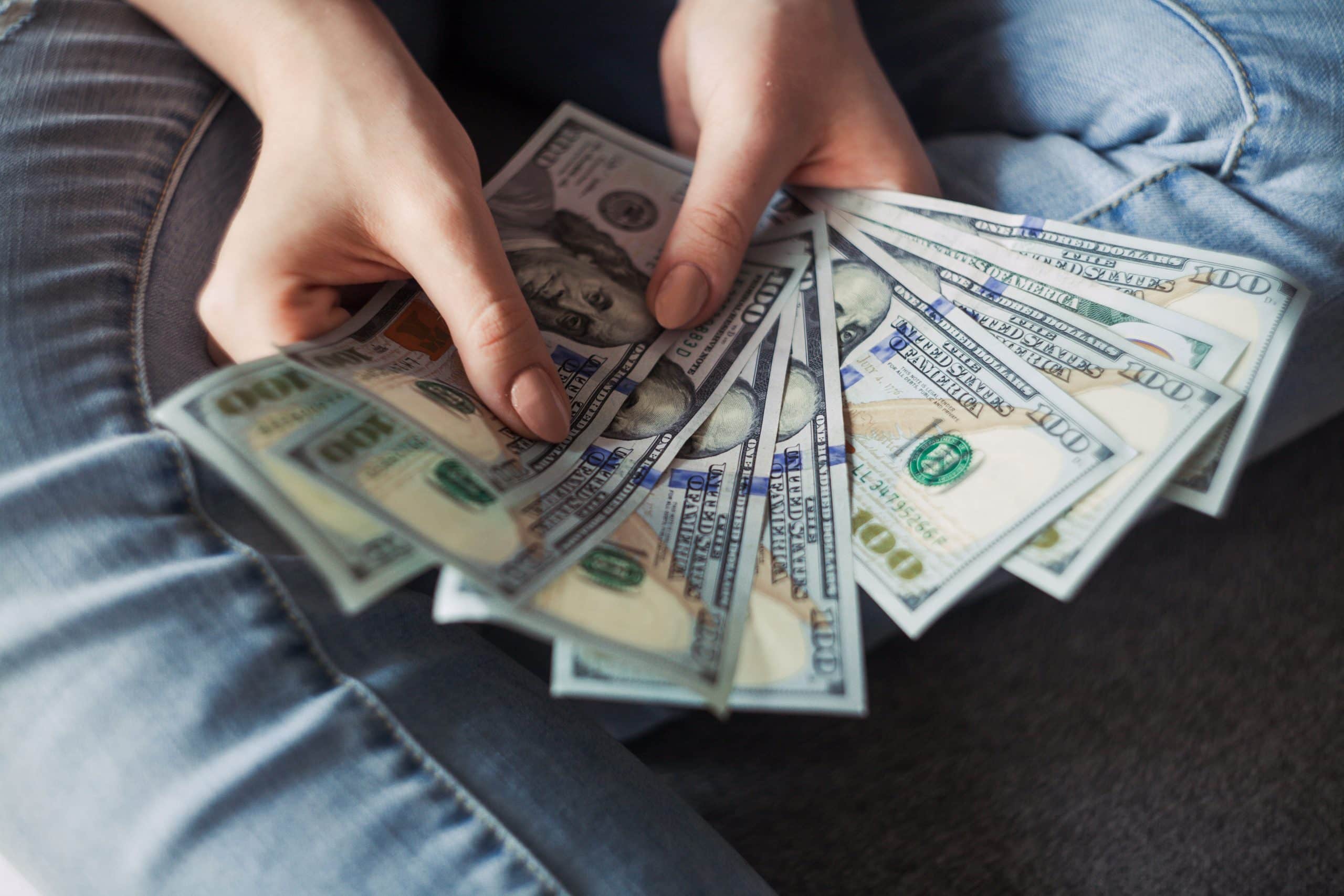 A closeup of a person wearing jeans, holding out 9 x 100 dollar bills in a fan shape.
