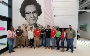A group of people standing in front of a mural of Katherine Johnson.