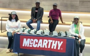 Group of people sitting around a table with construction inclusion week hats.