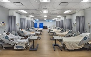 A room with rows of hospital beds and practice dummies for healthcare education.