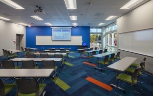 A classroom with rows of tables and three chairs at each table.